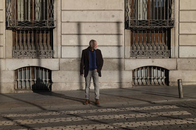 Adult man in suit crossing street against stone wall with sunlight and shadow