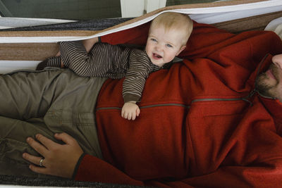 Overhead portrait of cute cheerful son with father lying in hammock