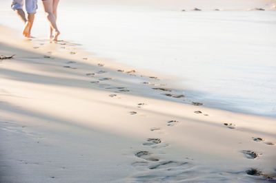 Low section of couple walking on shore at beach