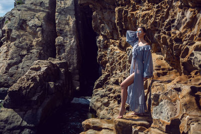 Fashionable brunette woman in a gray dress stands on a cheese rock in the summer