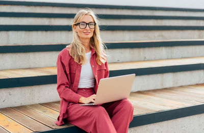 Portrait of young woman using laptop while sitting on steps