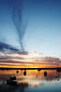 Boats moored in sea against sky during sunset