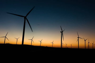 Silhouette wind turbines on field against sky during sunset