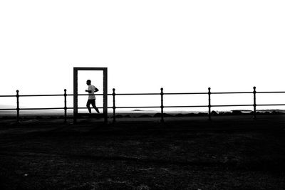 Silhouette man running on footpath against clear sky