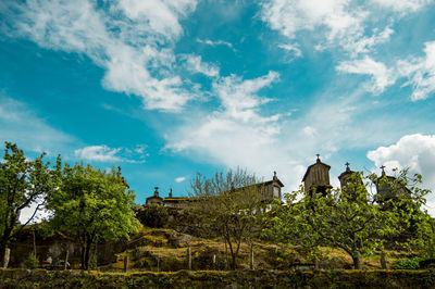 Low angle view of trees and chapels against cloudy sky