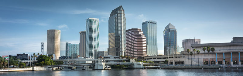 Modern buildings by river against sky in city