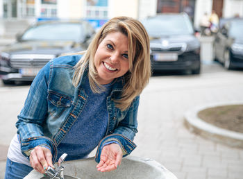 Woman with a beaming smile leaning on a fountain, dressed in denim