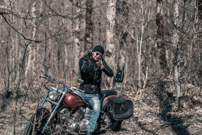 Full length of mid adult man sitting on motorcycle in forest