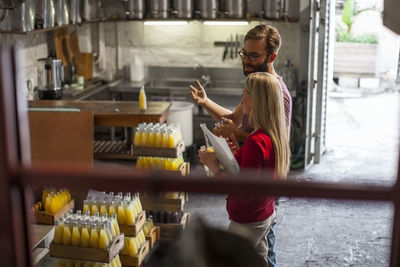 Man and woman discussing in warehouse with crates of juice bottles