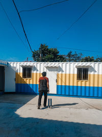 Full length rear view of man with umbrella against clear blue sky