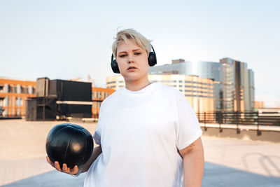 Portrait of teenage boy standing against sky in city
