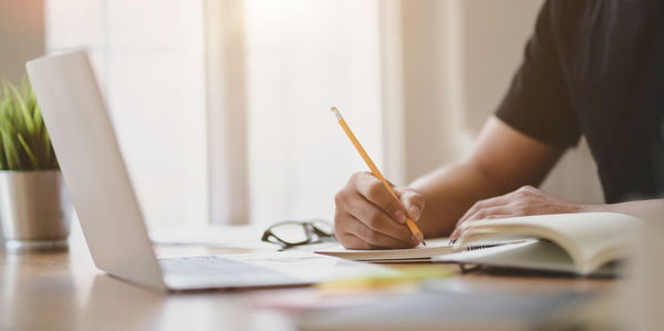 Midsection of businessman writing in diary on desk at office