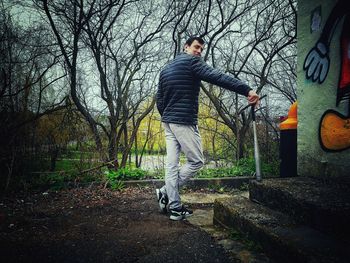 Side view of man standing by tree in forest