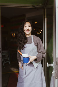 Happy female restaurant owner holding mug while standing at doorway