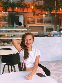 Portrait of a smiling young woman sitting on table at restaurant