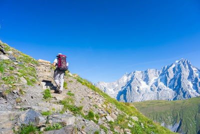 Rear view of hiker walking on mountain against clear blue sky