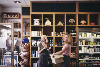 Female colleagues looking away while standing by rack in deli