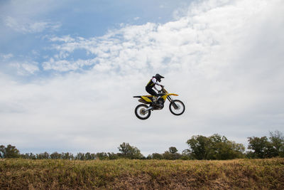 Rear view of man riding bicycle on field against sky