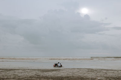 People riding on beach against sky