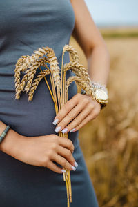 A woman in a blue dress gently cradles a bunch of golden wheat in her hands, symbolizing simplicity