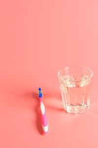 Toothbrush and a glass of water on a pink background