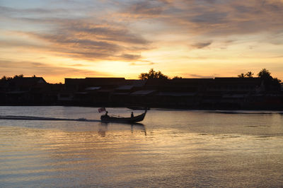 Silhouette man sitting on river against sky during sunset