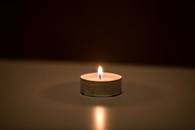Close-up of illuminated tea light candle in darkroom
