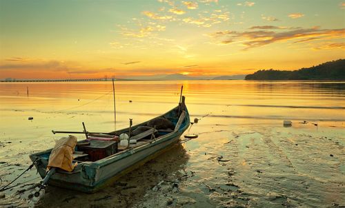 Boat moored on beach against sky during sunset