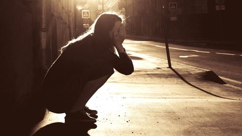 Side view of depressed woman sitting on sidewalk by road in city