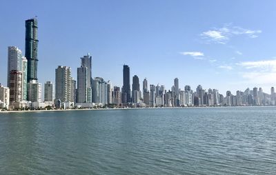 Sea by modern buildings in city against sky