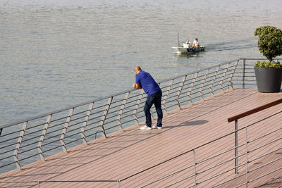 Rear view of man standing on pier by sea