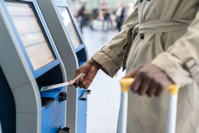 Midsection of woman using self check in kiosk at airport