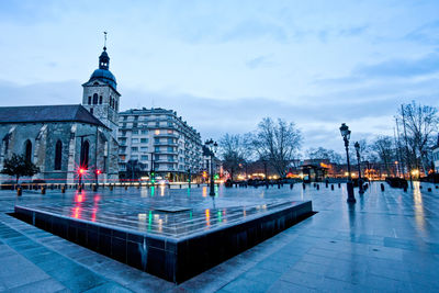 Illuminated buildings against cloudy sky