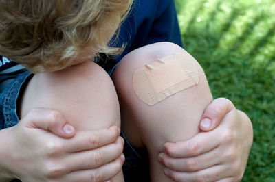 High angle view of boy with adhesive bandage on knee sitting on grass