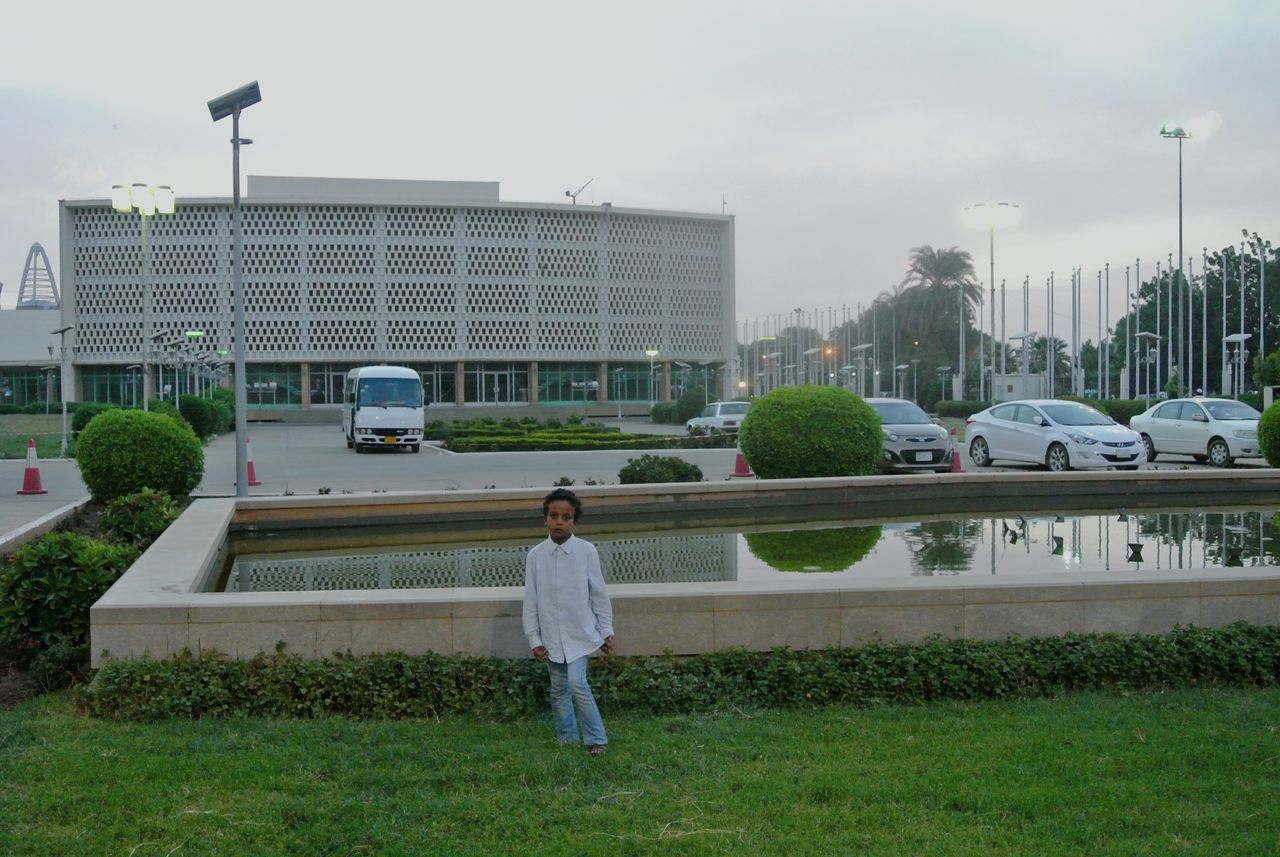 building exterior, full length, architecture, grass, casual clothing, built structure, rear view, lifestyles, leisure activity, sky, standing, walking, city, men, childhood, boys, day, outdoors