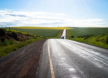 Car moving on road amidst field against sky