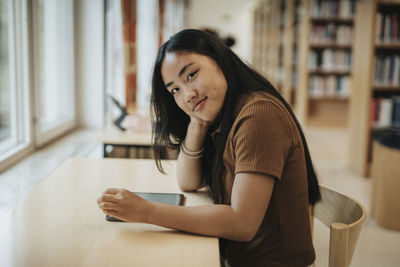 Portrait of smiling female student leaning at table in library