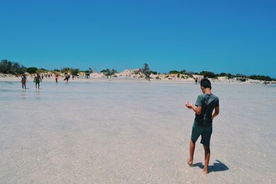 Full length of man on beach against clear blue sky