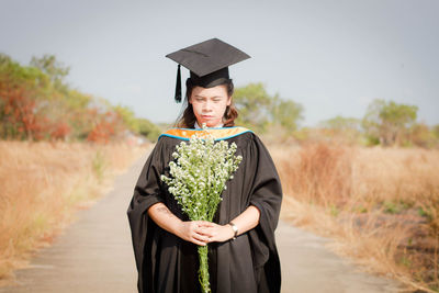 Student wearing graduation gown holding flowers on road