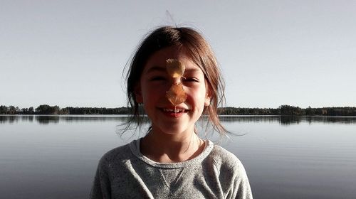 Portrait of girl with leaves on nose against lake and clear sky