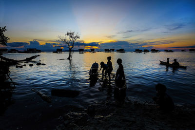 Silhouette children with boat in sea against sky during sunset