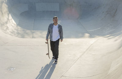 Man with skateboard walking on ramp in park