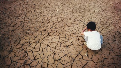 Rear view of boy crouching on cracked field