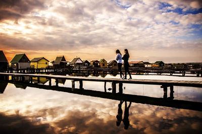 Silhouette people on pier over lake against sky during sunset