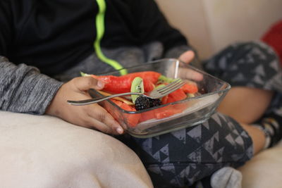 Midsection of boy eating fruits while sitting on sofa at home