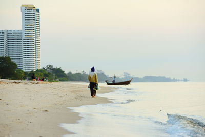 Full length rear view of fisherman holding net while walking on shore at beach