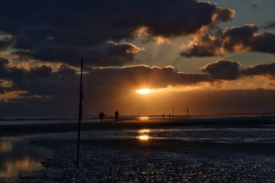 Silhouette man fishing on beach against sky during sunset