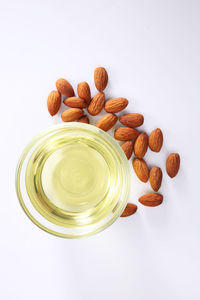 Close-up of cooking oil in bowl and almonds over white background