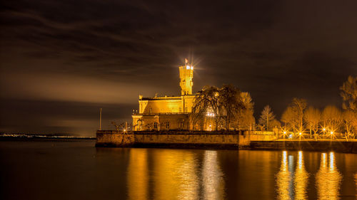 Illuminated building by river against sky at night