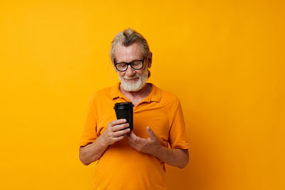 Senior man holding disposable cup against yellow background